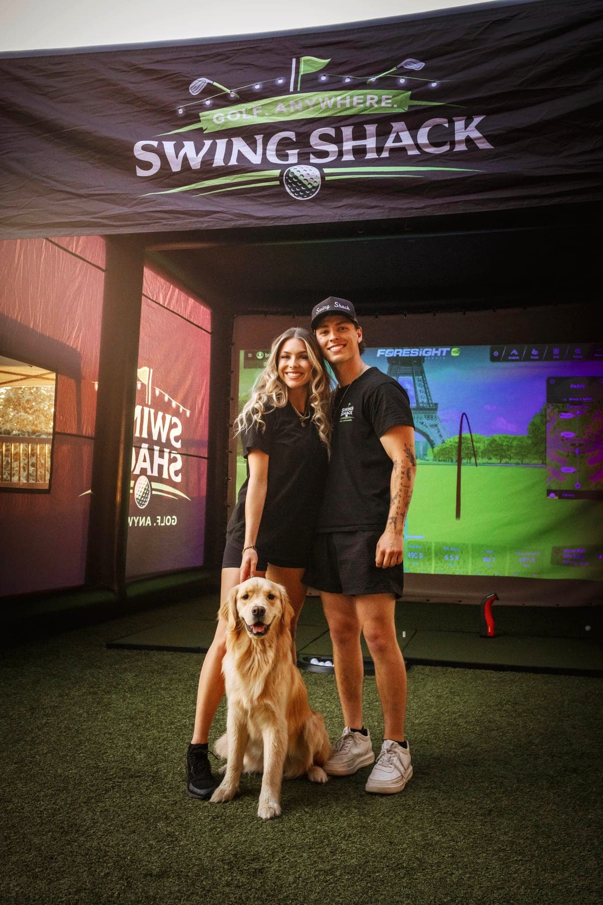 The Swing Shack owners and their golden retriever standing in front of the simulator showing a Paris golf course