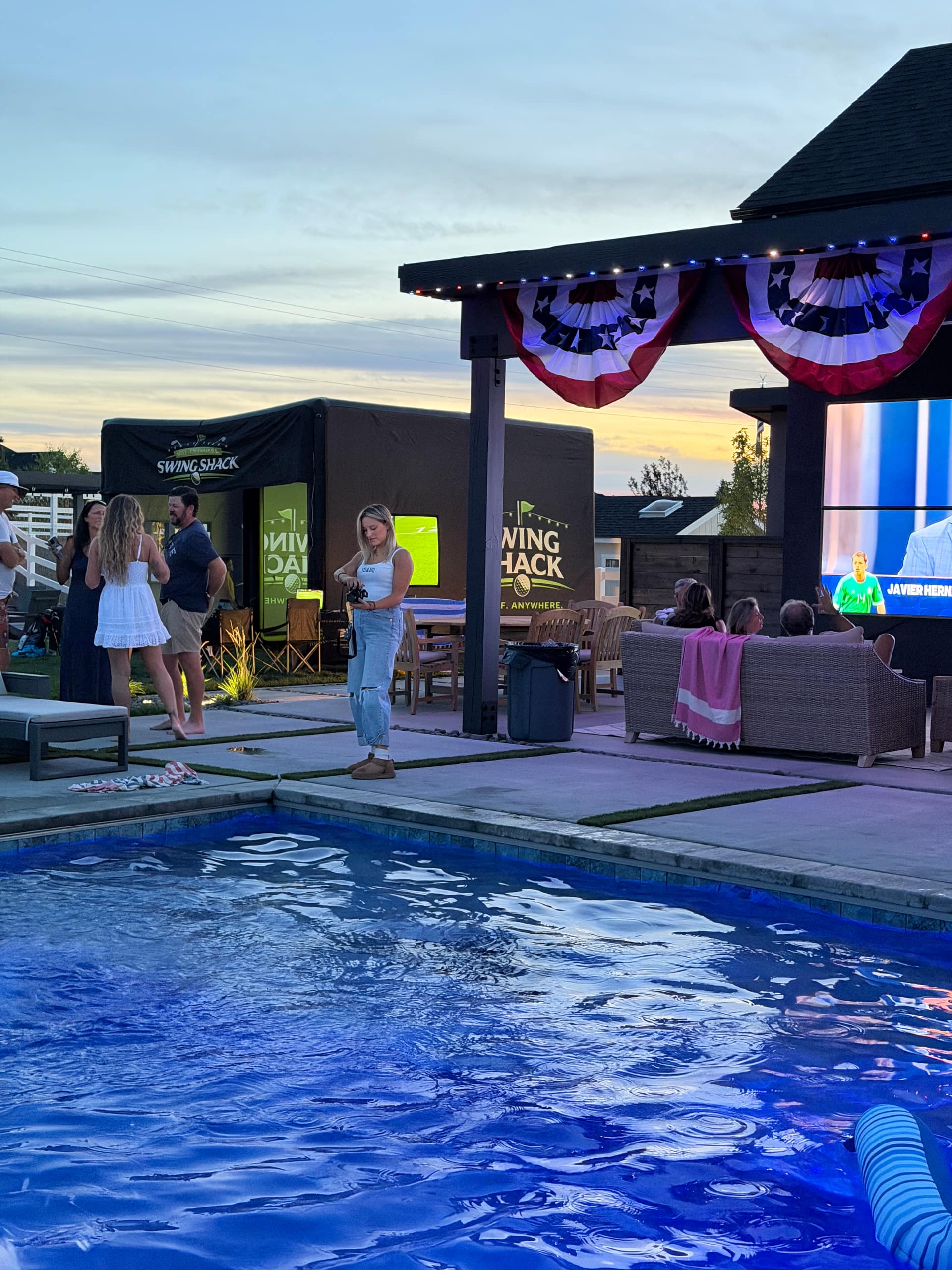 Guests at a summer pool party with red, white and blue bunting and the Swing Shack simulator set up beside the pool